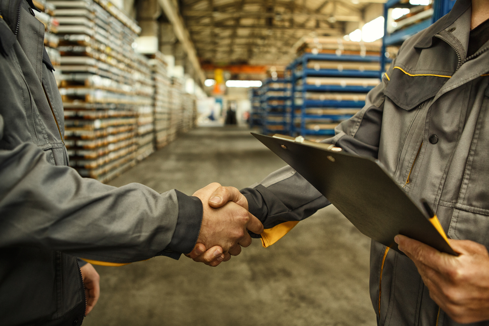 Two men shake hands in a factory, one is holding a clipboard – article about food safety compliance considerations in selecting supply partners