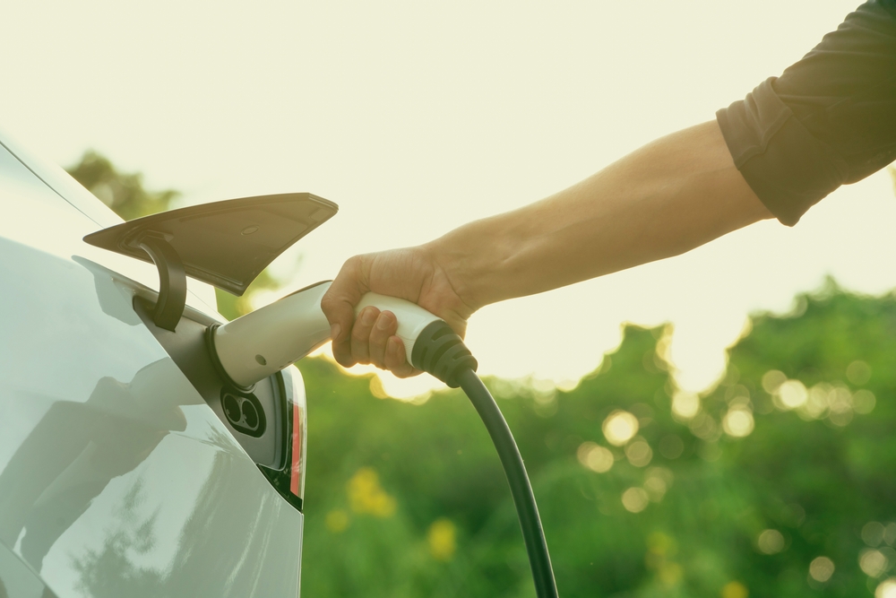 View of a man’s hand as he charges his electric vehicle - article about immersion cooling oils and EV innovation