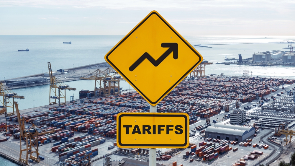 sign that says Tariffs with an arrow going upward against a backdrop of shipping containers - article about energy tariffs and how oil suppliers can help stabilize costs