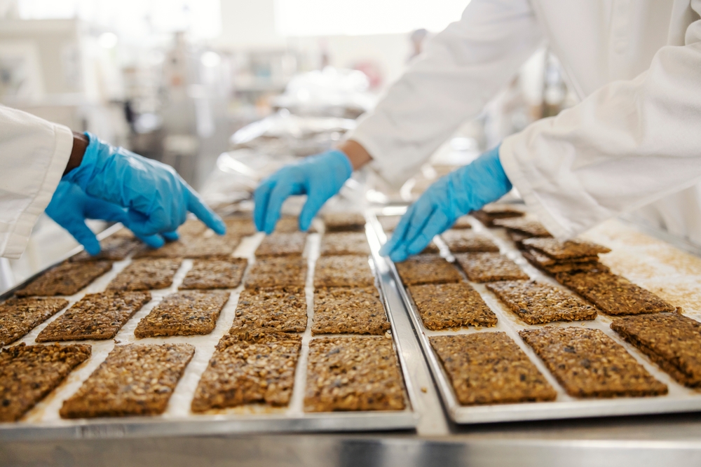 Food Production with SQF Certified Suppliers food industry workers collecting baked fresh snacks from tray at facility with an SQF-certified supply chain