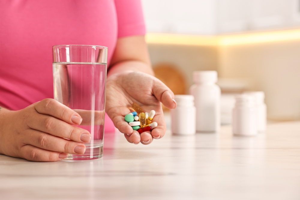 Food-Grade Oils for Supplement Manufacturing woman holding pile of dietary supplements and glass with water at marble countertop in kitchen, closeup - article about food-grade oils used in supplement manufacturing