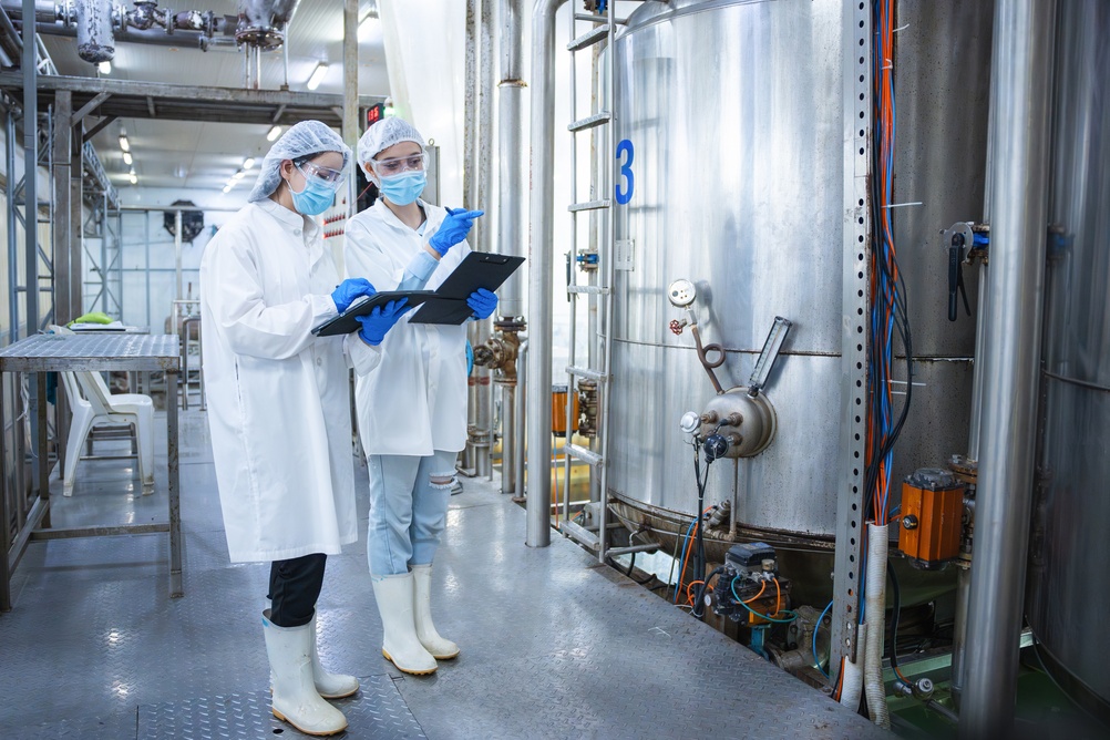 2 masked female engineers inspecting industrial storage tank and piping system in a gel factory - article about process oil supplier solving factory mineral oil haze issue